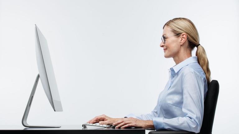 Woman sitting at an iMac with a relaxed, upright, natural head position wearing Shamir Computer lenses